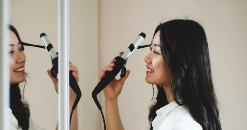 woman looking into mirror, smiling, using a curling iron to curl her hair