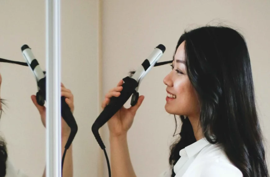 woman looking into mirror, smiling, using a curling iron to curl her hair