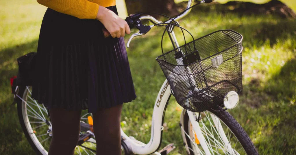 close up of person wearing black pleated skirt, black tights, yellow top, holding onto a bike by the handles