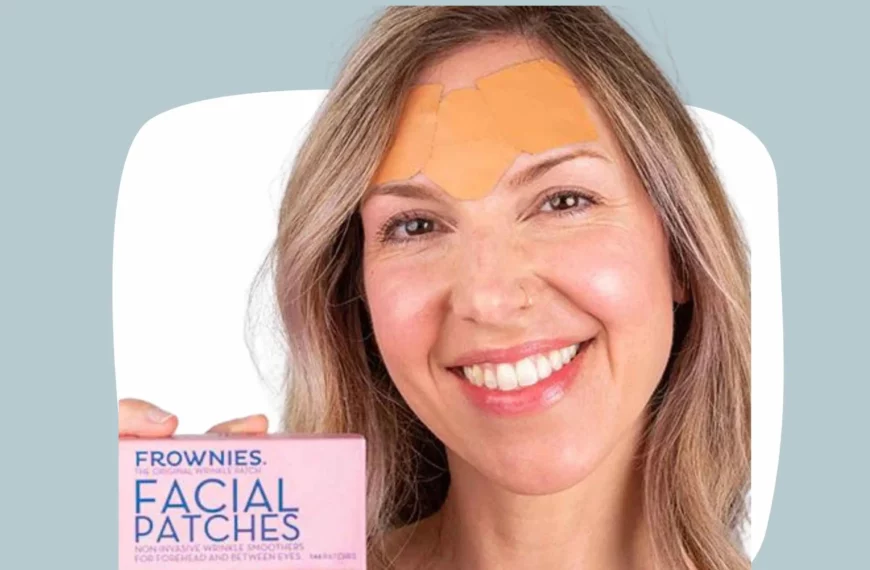 head shot of woman smiling, wearing Frownies facial patches on forehead, and holding a box of Frownies facial patches