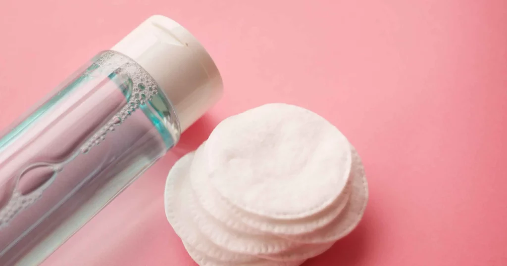 micellar water or toner in clear bottle lying next to round cotton pads