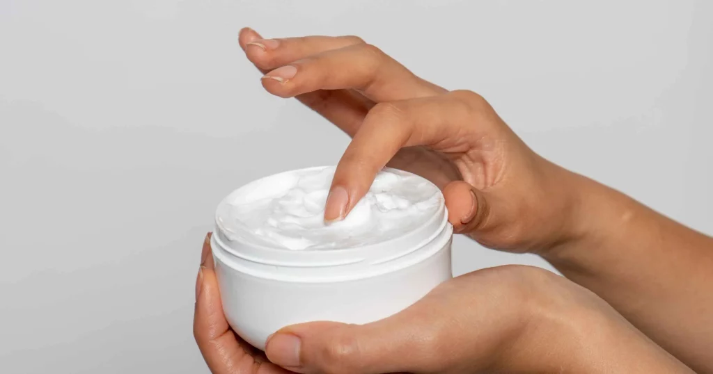 close up of person's hands dipping finger into container of lotion