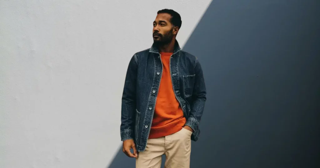 man looking off camera, wearing orange shirt, tan pants, and jean jacket from Taylor Stitch