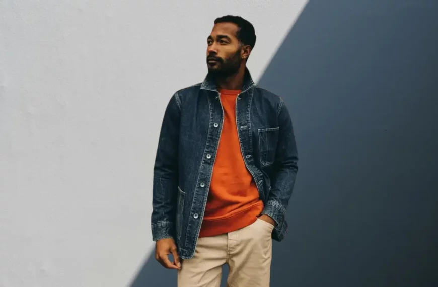 man looking off camera, wearing orange shirt, tan pants, and jean jacket from Taylor Stitch