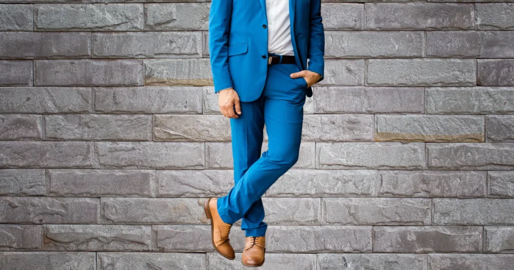 person leaning against gray wall wearing blue suit brown shoes