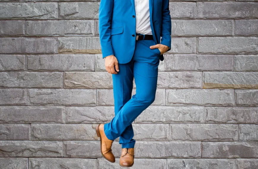 person leaning against gray wall wearing blue suit brown shoes