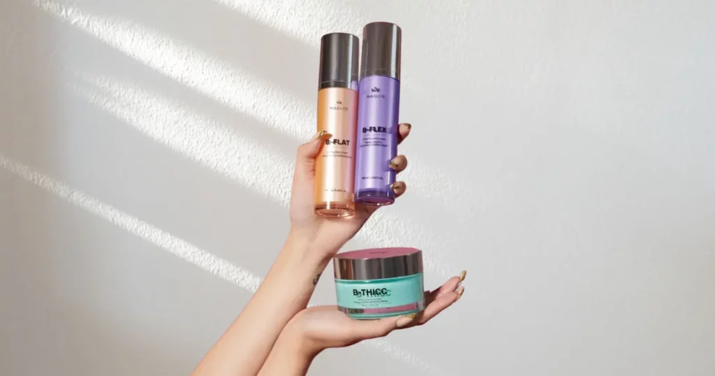 two hands holding up Maelys Cosmetics products in orange, purple, and green containers