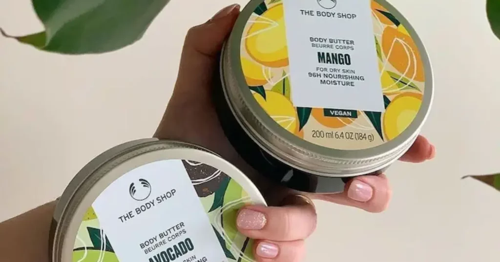 persons hand holding two jars of the body shop body butters