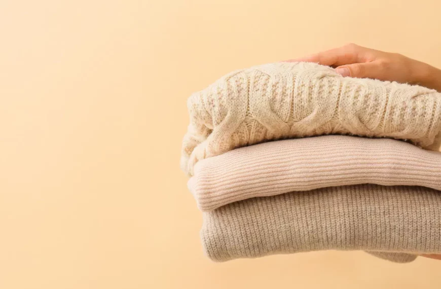 pair of hands holding out a stack of neutral colored polyester sweaters