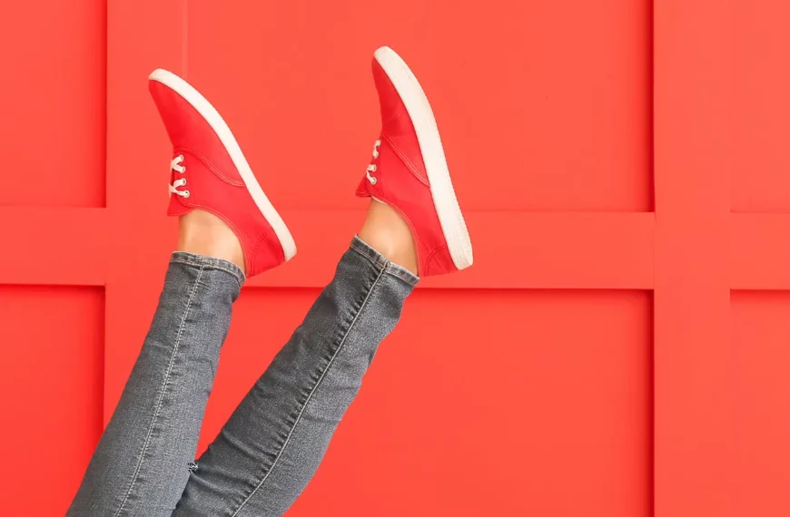 person's feet in the air, wearing red shoes and blue jeggings against an orange-red background