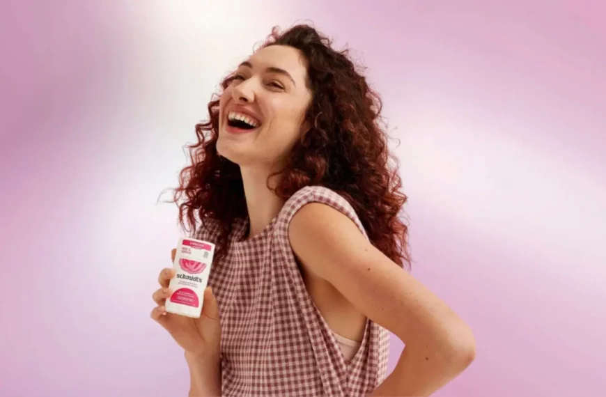 woman with curly hair looking off camera, smiling, holding Schmidt's natural deodorant