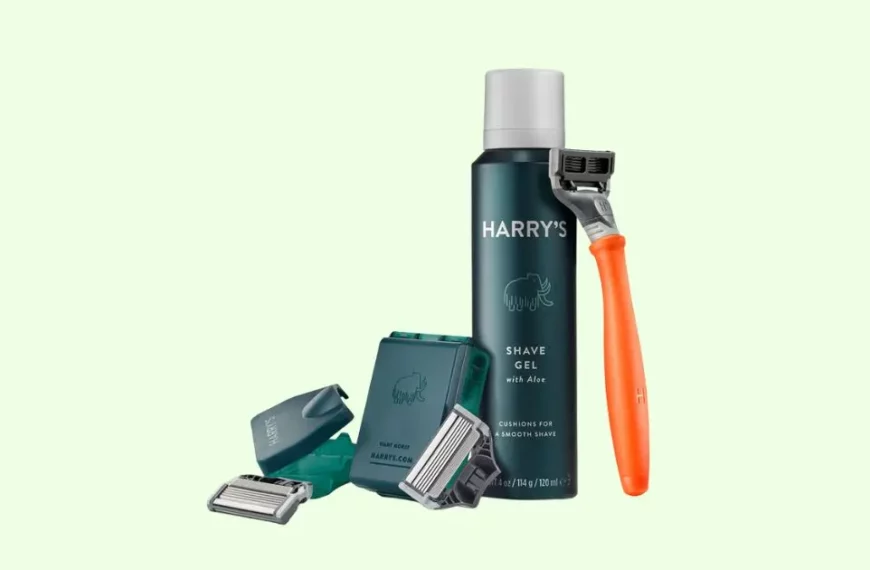 harry's razor bundle that showcases the brand's Truman razor with orange colored handle, shave gel, two replacement blades with a holding box, and a razor cover. Photo has a pastel green background.